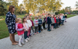 Dzieci stoją wraz z opiekunka na chodniku przy przedszkolu