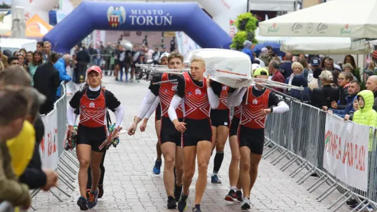 Wioślarze AZS UMK biegnący z kajakiem przez Rynek Staromiejski w Toruniu