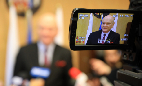 Prezydent Michał Zaleski w obiektywie kamery telewizyjnej przed mikrofonami dziennikarzy.