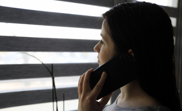 Dziewczyna rozmawiająca przez telefon komórkowy przy oknie z żaluzjami