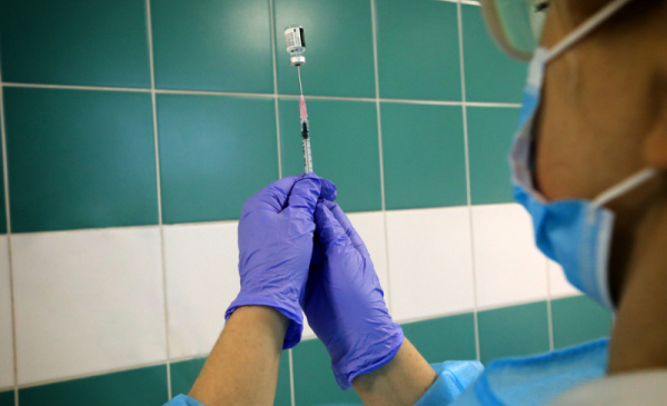 Na zdjęciu widać dłonie pielęgniarki w rękawiczkach, trzymające strzykawkę ze szczepionką
