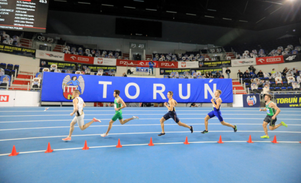 Na zdjęciu: zawodnicy biegną po bieżni w hali sportowej