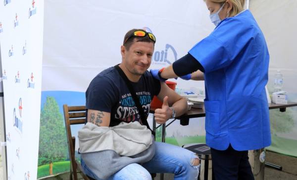 Na zdjęciu uśmiechnięty mężczyzna jest szczepiony i pokazuje kciuka w górę
