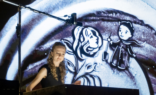 Aktorka teatru Piaskowa Magia na tle ekranu z Małym Księciem podczas spektaklu