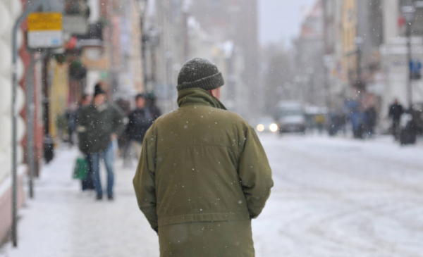 Na zdjęciu widać mężczyznę w czpce i grubej kurtce, idącego zaśnieżoną ulicą