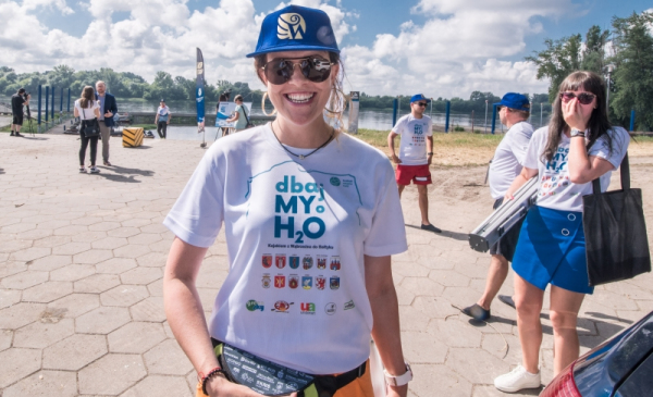 Na zdjęciu dziewczyna z koszulką Dbajmy o H2O uśmiecha się na przystani w Toruniu