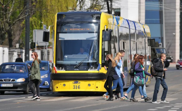 Zdjęcie przedstawia tramwaj MZK i młodych ludzi przechodzących przez przejście dla pieszych