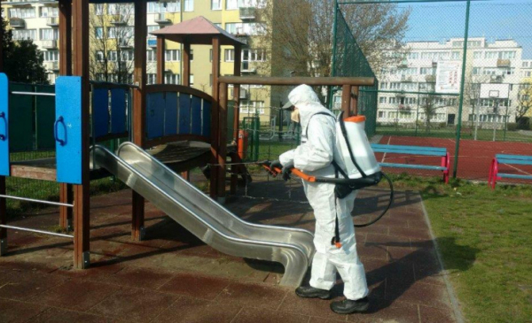 Pracownik ubrany w kombinezon ochronny przeprowadza dezynfekcję zjeżdżalni na placu zabaw