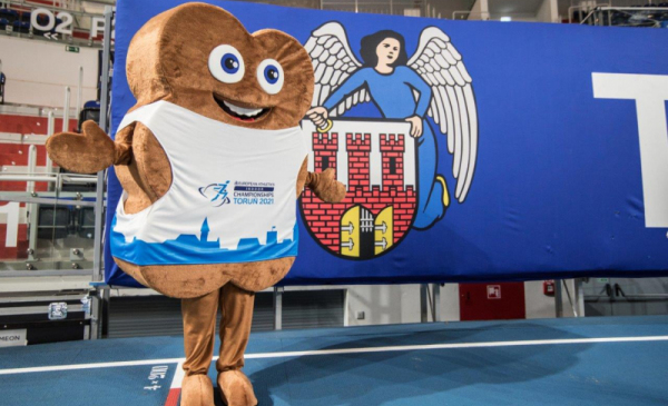 Na zdjęciu widac maskotkę Halowych Mistrzostw Europy w Lekkiejatletyce Toruń 2021 w kształcie katarzynki, w tle herb Torunia