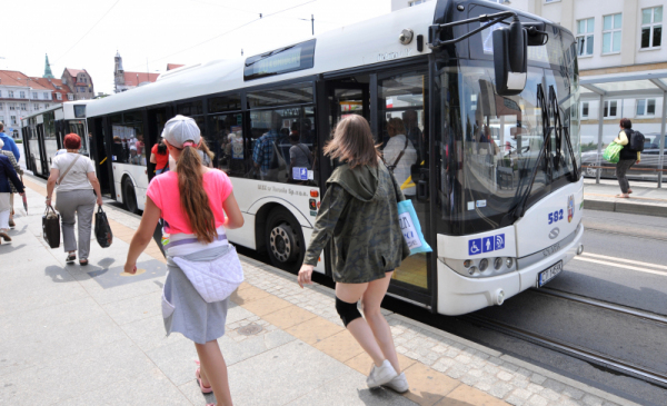 Młode dziewczęta idą wzdłuż przystanku autobusowego, w tle biały autobus miejski