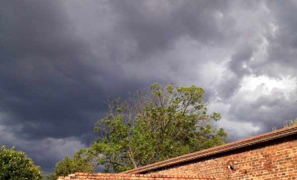 Na zdjęciu: granatowe burzowe chmury nad drzewem i ceglanym murem