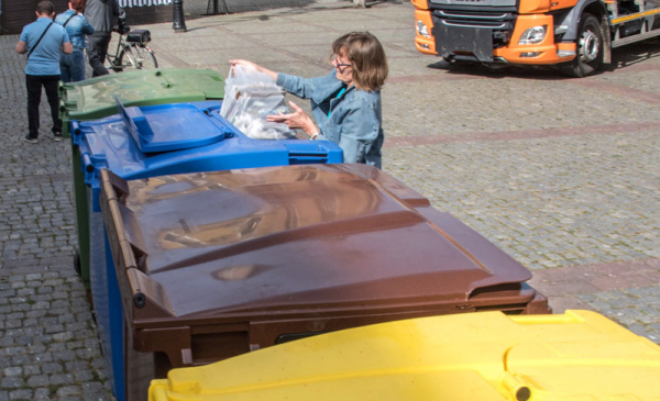 Rząd kolorowych pojemników na odpady i kobieta wyrzucajaca śmieci