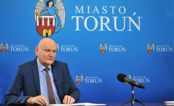 Prezydent Michał Zaleski podczas sesji Rady Miasta przeprowadzonej on-line siedzi na tleniebieskiej ścianki z herbem Torunia