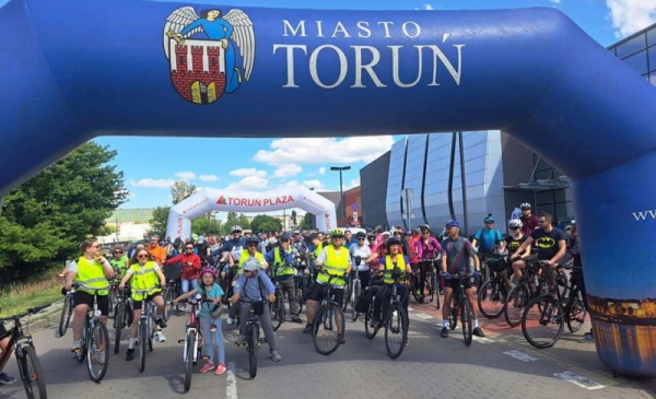 Na zdjęciu: startują rowerzyści, nad nimi herb miasta Torunia