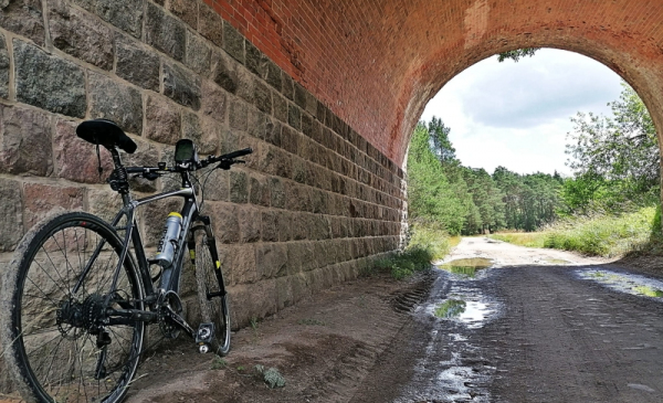 Na zdjęciu rower oparty o mur pod wiaduktem