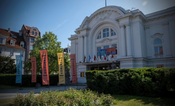 Na zdjęciu: biały budynek Teatru im. Wilama Horzycy, obok stoją flagi informujące o odbywającym się festiwalu Kontakt