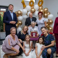 Wspólne zdjęcie gości uroczystości z jubilatką pod napisem 100