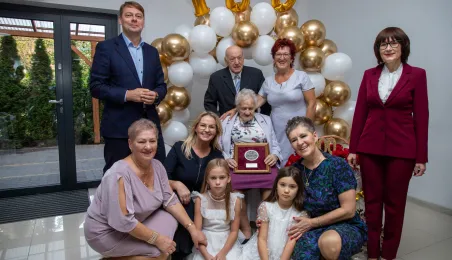 Wspólne zdjęcie gości uroczystości z jubilatką pod napisem 100