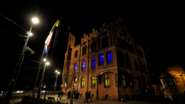 Na zdjęciu budynek urzędu miasta i okna podświetlone na niebiesko-żółto