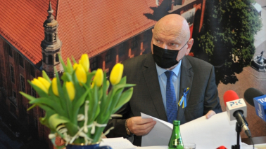 Na zdjęciu prezydent Torunia Michał Zaleski mówi podczas konferencji, przed nim stoi wazon z żółtymi tulipanami