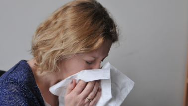 Na zdjęciu kobieta wydmuchuje nos w chusteczkę higieniczną
