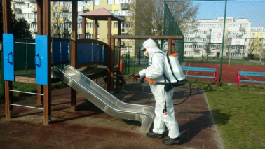 Pracownik ubrany w kombinezon ochronny przeprowadza dezynfekcję zjeżdżalni na placu zabaw