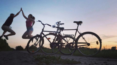 Na zdjęciu: ludzie przybijający piątkę i dwa rowery na tle zachodu słońca