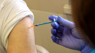 Na zdjęciu zbliżenie na strzykawkę ze szczepionką podczas podawania zastrzyku - widać ramię i wkłutą igłę