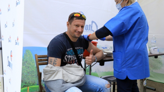 Na zdjęciu uśmiechnięty mężczyzna jest szczepiony i pokazuje kciuk w górę