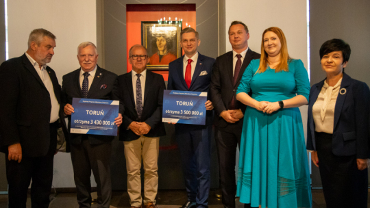 Na zdjęciu: Zbigniew Fiderewicz i Adrian Mól, zastępcy prezedenta Torunia, stoją wśród przedstawicieli rządu i posłów i pokazują promesy na dofinansowanie