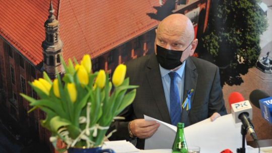 Na zdjęciu prezydent Torunia Michał Zaleski mówi podczas konferencji, przed nim stoi wazon z żółtymi tulipanami