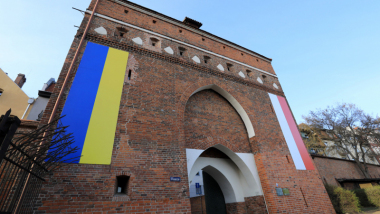 Na djęciu: brama klasztorna z dwiema flagami: ukraińską i polską