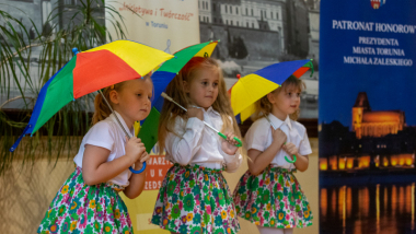 Na zdjęciu: trzy dziewczynki z parasolkami występują na scenie