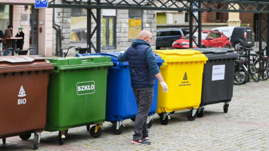 Zdjęcie przedstawia mężczyznę na tle pojemników na odpady.