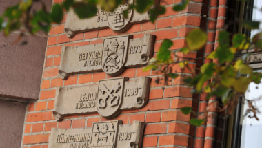 Zdjęcie przedstawia tablice miast bliźniaczych na ścianie toruńskiego Urzędu Miasta