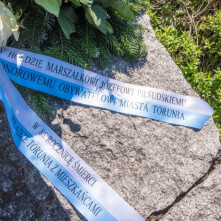 Na zdjęciu biało-błękitna wstęga na pomniku z napisem W hołdzie marszałkowi Józefowi Piłsudskiemu, Honorowemu Obywatelowi Miasta Torunia w 86. rocznicę śmierci władze Torunia z mieszkańcami