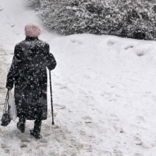 Starsza pani z laską idąca przez zaśnieżony chodnik