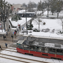 Widok na czerwony tramwaj i zaśnieżoną ulicę Wały gen. Sikorskiego w Toruniu