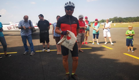 Na zdjęciu uczestnik historycznego rajdu rowerowego "Śladem toruńskich dróg do wolności" stoi na Lotnisku Aeroklubu Pomorskiego i trzyma w rękach nagrodę