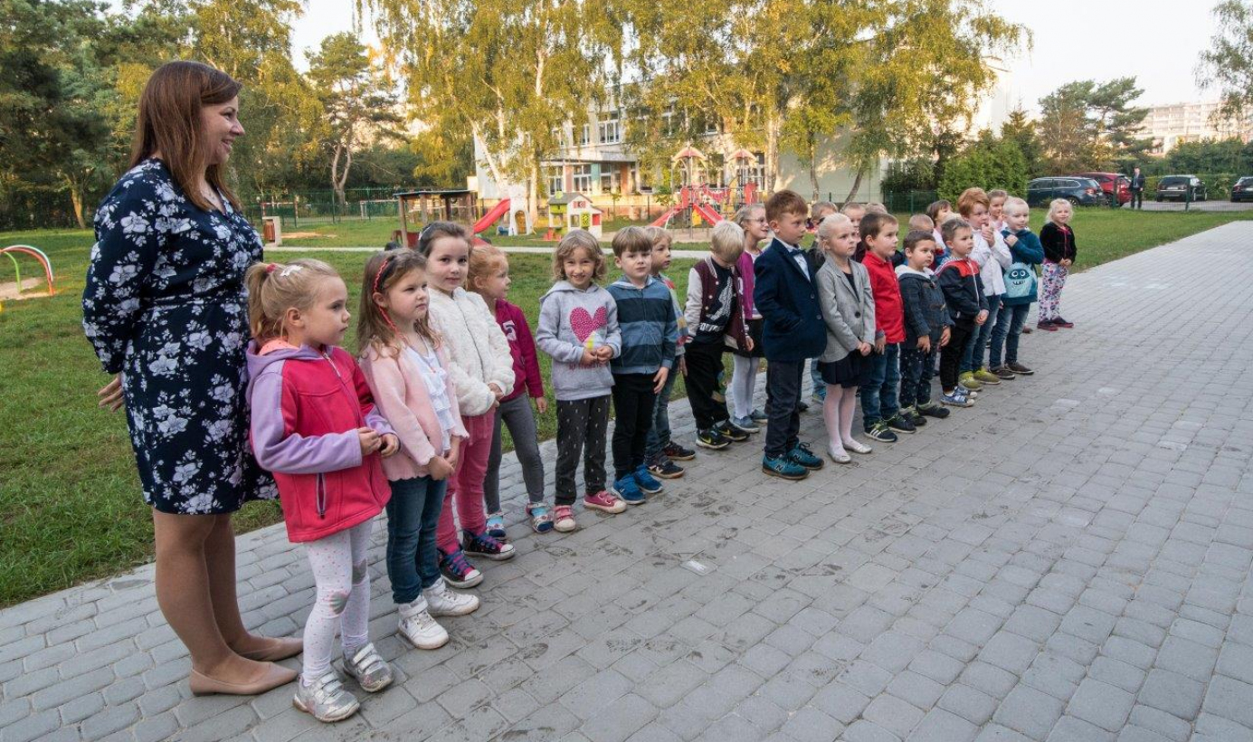 Dzieci stoją wraz z opiekunka na chodniku przy przedszkolu